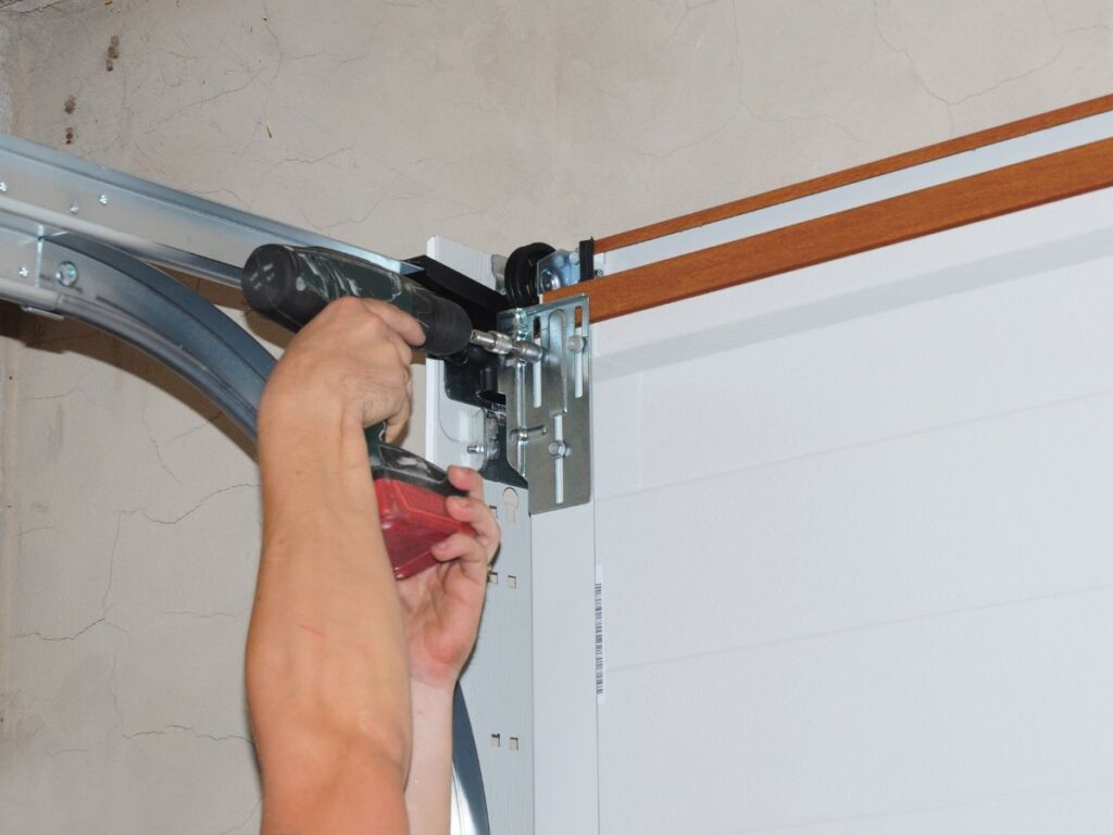 Technician installing garage door hardware with a power drill.