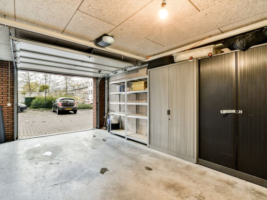 Clean garage interior with open door, storage shelves, and cabinets.