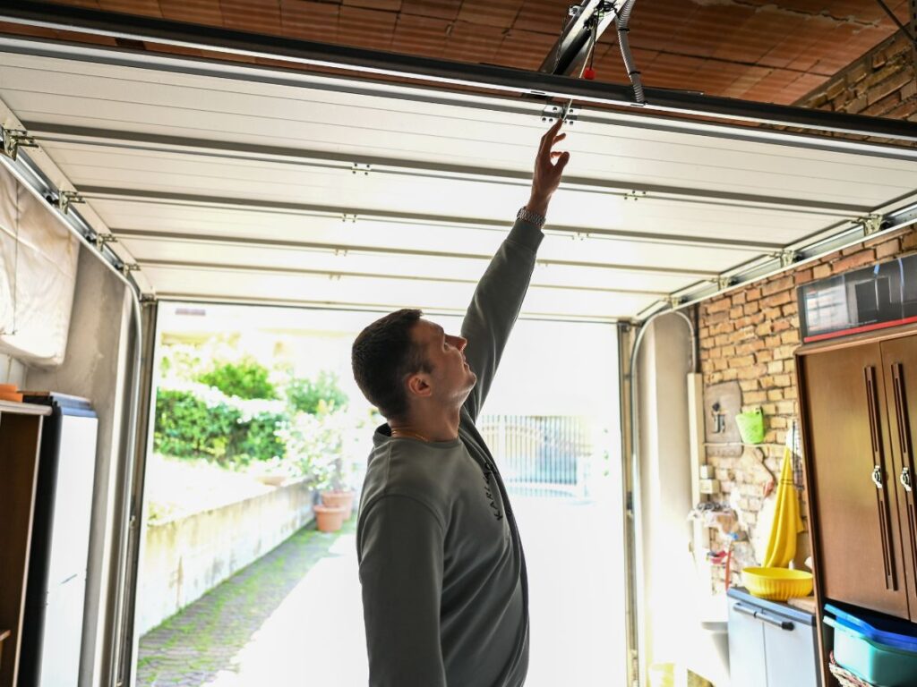 Homeowner reaching up to inspect or test a garage door opener.