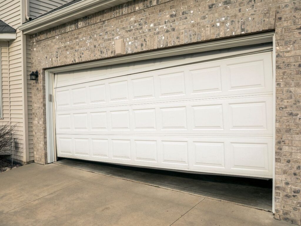 Garage door stuck crooked and partially open on a home exterior.